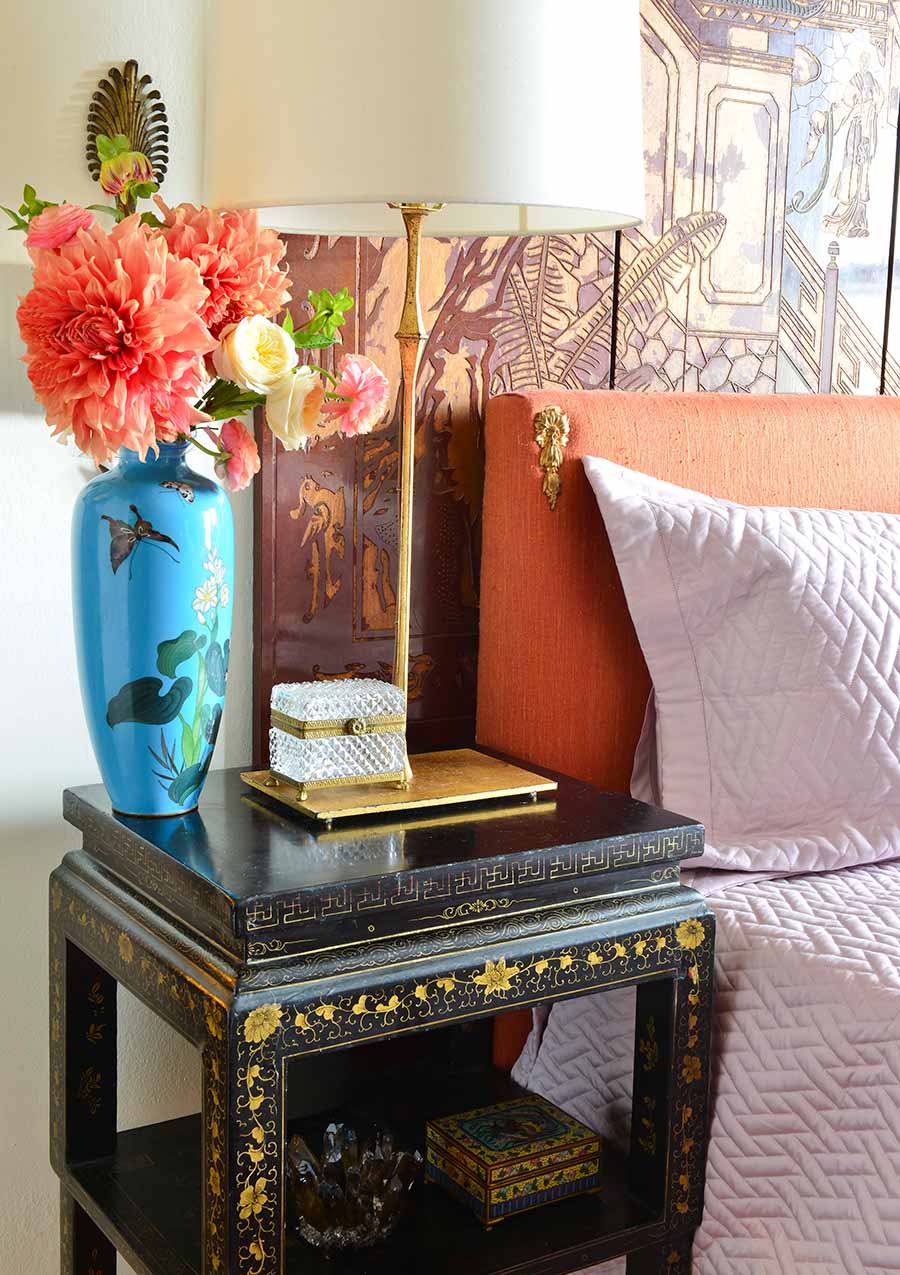Bedroom end table of painted black lacquer with blue vase and gilded lamp